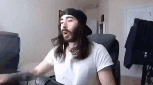A Man With Long Hair And A Beard Is Wearing A White Shirt And A Black Hat . GIF