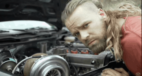 A Man With Long Hair And A Beard Is Working On A Car GIF