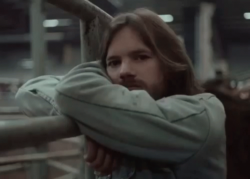 A Man With Long Hair And A Beard Leans Against A Metal Railing . GIF