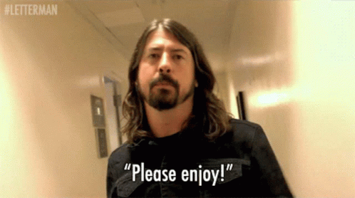 A Man With Long Hair And A Beard Says " Please Enjoy " In A Hallway GIF