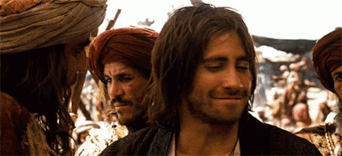 A Man With Long Hair And A Beard Smiles In Front Of A Group Of Men GIF