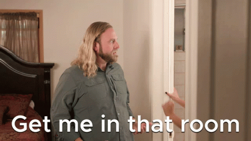 A Man With Long Hair And A Beard Stands In Front Of A Door With The Words Get Me In That Room Below Him GIF