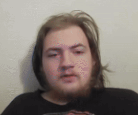 A Man With Long Hair And A Beard Wearing A Black Shirt Looks At The Camera GIF