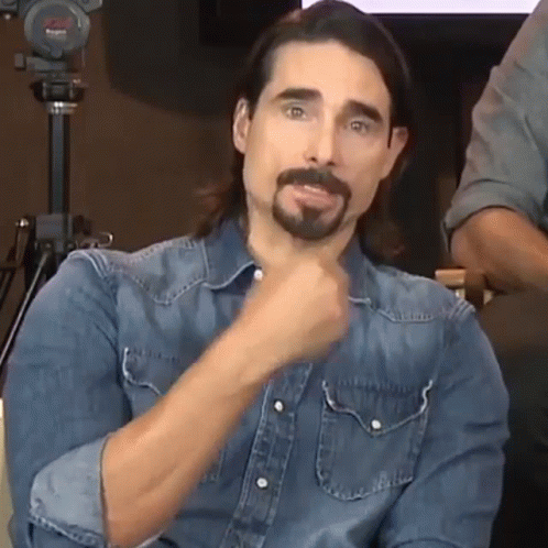 A Man With Long Hair And A Beard Wearing A Denim Shirt Is Making A Funny Face . GIF