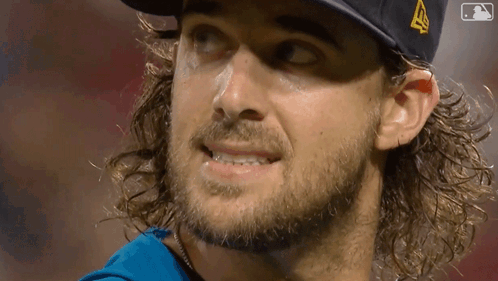 a man with long hair and a beard wearing a hat with a mlb logo on it
