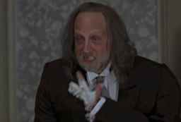 A Man With Long Hair And A Beard Wearing A Suit And Tie Smoking A Cigarette GIF