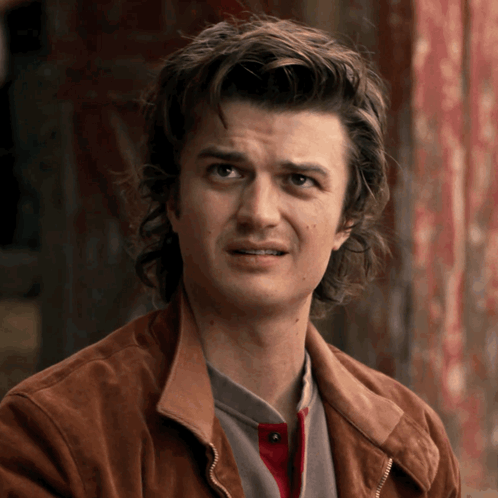 A Man With Long Hair And A Brown Jacket Is Making A Funny Face GIF