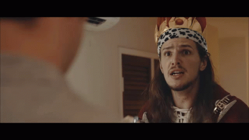A Man With Long Hair And A Crown On His Head Is Talking To Another Person GIF