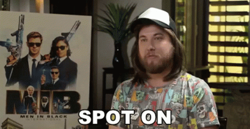 A Man With Long Hair And A Hat Is Standing In Front Of A Men In Black Poster . GIF
