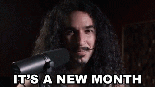 A Man With Long Hair And A Mustache Is Standing In Front Of A Microphone And Saying `` It 'S A New Month '' GIF