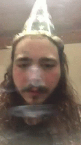 A Man With Long Hair And A Mustache Is Wearing A Cone Hat . GIF