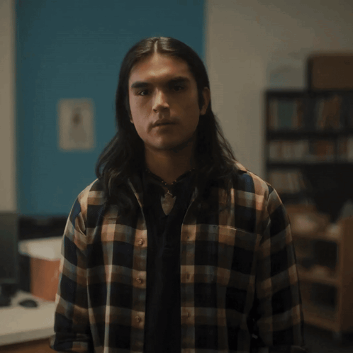 A Man With Long Hair And A Plaid Shirt Looks At The Camera GIF