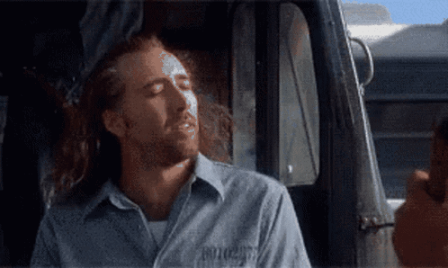 A Man With Long Hair And A Shirt That Says ' Prisoner ' On It Is Sitting In A Car GIF
