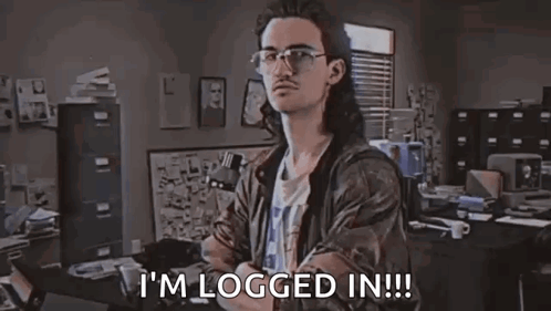 A Man With Long Hair And Glasses Is Sitting At A Desk In An Office . GIF