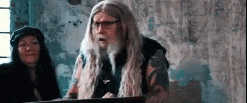 A Man With Long Hair And Glasses Is Standing In Front Of A Podium . GIF