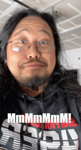 A Man With Long Hair And Glasses Is Wearing A Shirt That Says " Mmmmm " GIF
