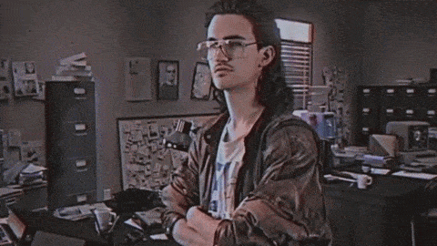 A Man With Long Hair And Glasses Stands In Front Of A Sign That Says Hackman GIF