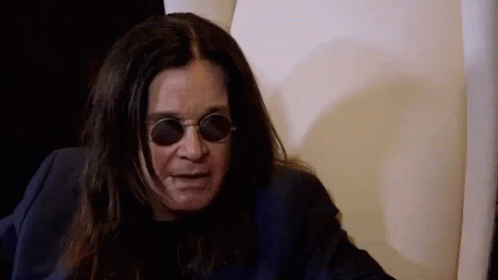 A Man With Long Hair And Sunglasses Is Sitting In A Chair . GIF