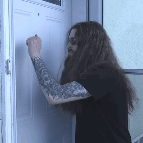 a man with long hair and tattoos knocks on a door