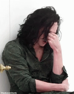 A Man With Long Hair Covering His Face With His Hand GIF