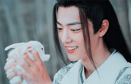 A Man With Long Hair Holds A Small White Rabbit In His Hands GIF