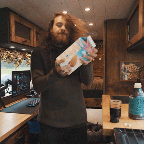 A Man With Long Hair Is Holding A Box Of Cookies In His Hands GIF