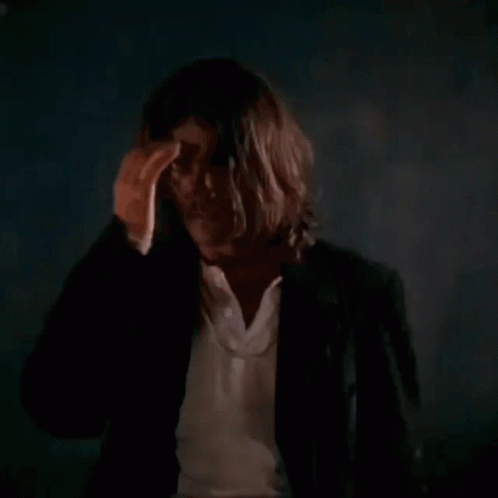 A Man With Long Hair Is Holding A Gun In His Hand GIF