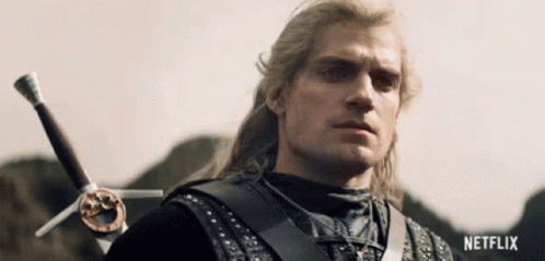 a man with long hair is holding a sword in his right hand and looking at the camera .