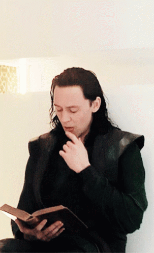 A Man With Long Hair Is Reading A Book While Sitting Down GIF