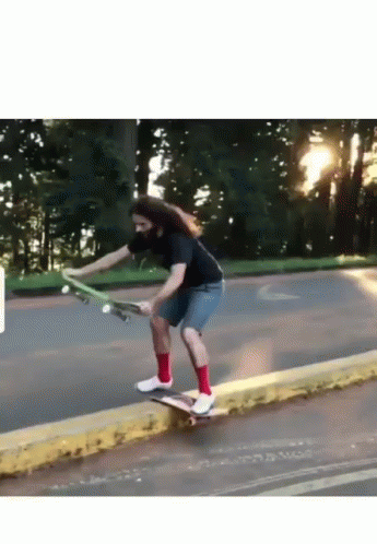 A Man With Long Hair Is Riding A Skateboard Down A Street GIF