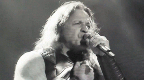 A Man With Long Hair Is Singing Into A Microphone In A Black And White Photo GIF