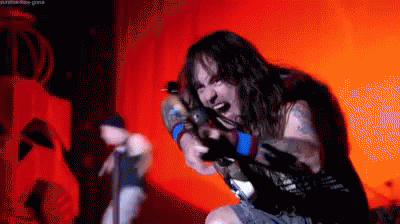 A Man With Long Hair Is Singing Into A Microphone In A Dark Room GIF