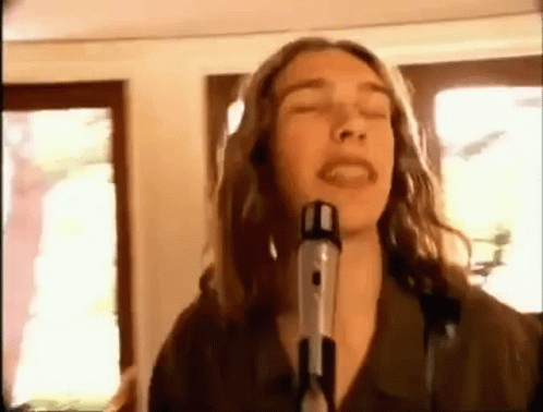 a man with long hair is singing into a microphone in a room .