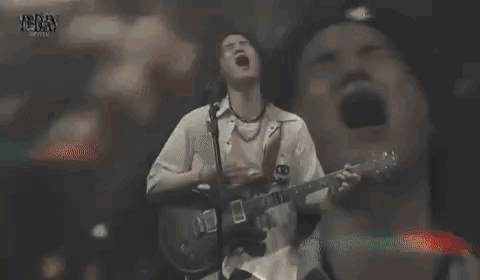 A Man With Long Hair Is Singing Into A Microphone While Making A Funny Face . GIF