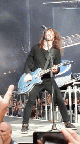 A Man With Long Hair Is Singing Into A Microphone While Playing A Guitar GIF