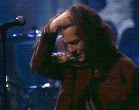 a man with long hair is singing into a microphone while touching his nose .
