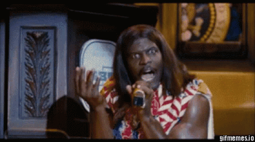 A Man With Long Hair Is Singing Into A Microphone While Wearing A Colorful Shirt . GIF