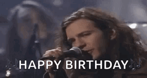 A Man With Long Hair Is Singing Into A Microphone With The Words `` Happy Birthday '' . GIF