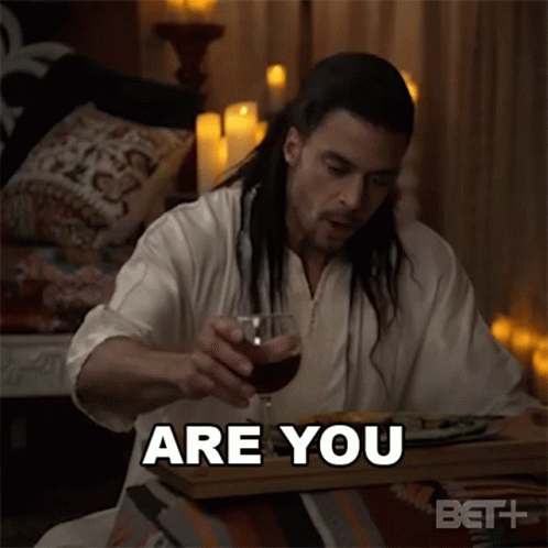 A Man With Long Hair Is Sitting At A Table With A Glass Of Wine And Says " Are You " GIF