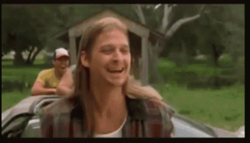 A Man With Long Hair Is Sitting In A Car Laughing . GIF
