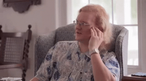 A Man With Long Hair Is Sitting In A Chair Talking On A Cell Phone . GIF