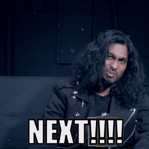 A Man With Long Hair Is Sitting Next To A Sign That Says Next GIF