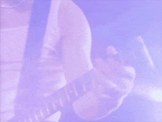 A Man With Long Hair Is Smiling And Looking At The Camera While Playing A Guitar . GIF
