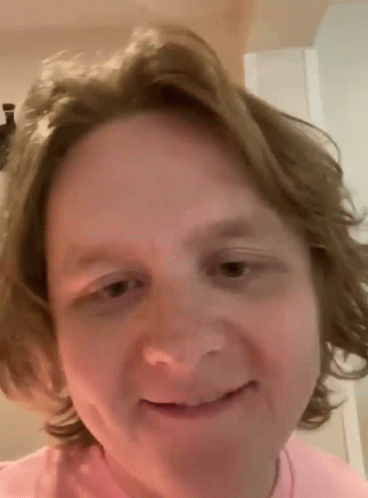 A Man With Long Hair Is Smiling And Wearing A Pink Shirt GIF