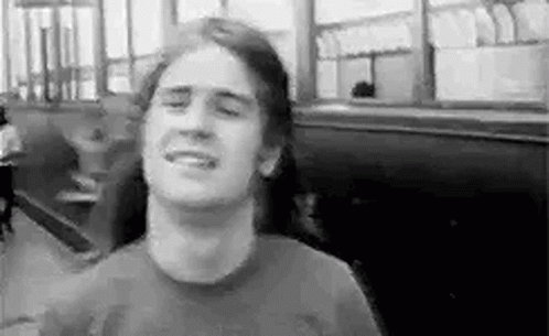 A Man With Long Hair Is Smiling In A Black And White Photo While Sitting In A Restaurant . GIF