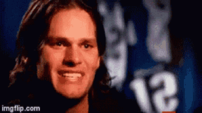 A Man With Long Hair Is Smiling In Front Of A Blue Background With The Number 12 Visible . GIF