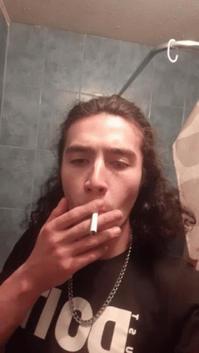 A Man With Long Hair Is Smoking A Cigarette While Wearing A Black Shirt That Says T2u GIF