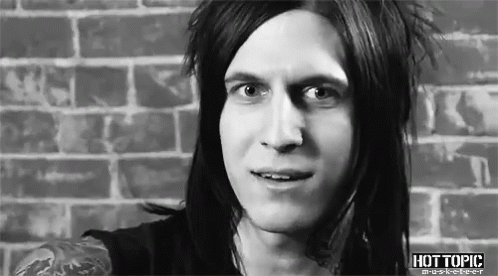 A Man With Long Hair Is Standing In Front Of A Brick Wall And Smiling . GIF