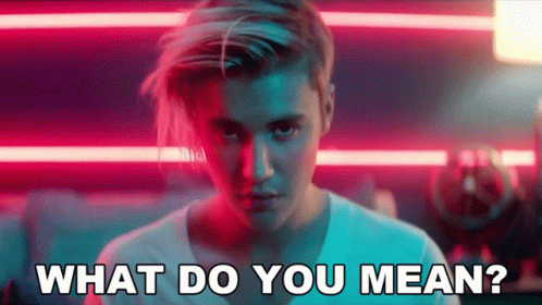 A Man With Long Hair Is Standing In Front Of A Neon Sign And Says What Do You Mean . GIF
