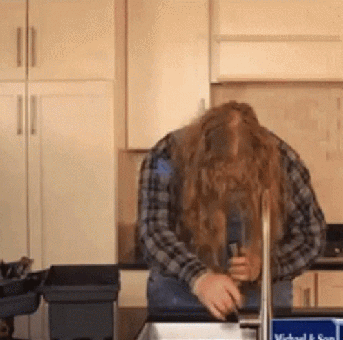 A Man With Long Hair Is Washing His Hands In A Sink . GIF